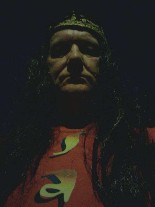 STEViE ZiPP wearing a long dark wig and fezz hat against a dark background