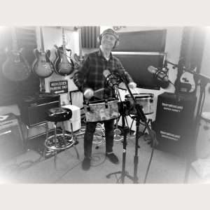 STEViE ZiPP wearing headphones in the studio whilst playing a drum