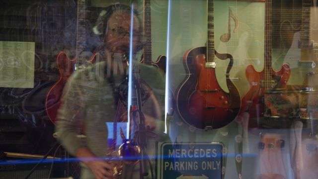 Tom O Martin playing sax behind a glass window with abstract reflections