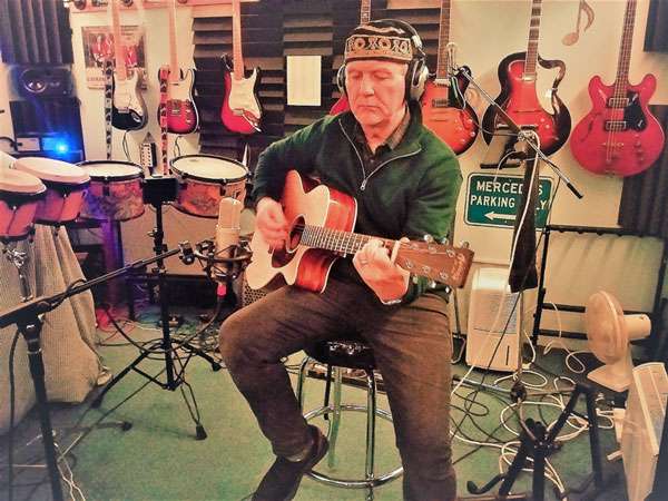 STEViE ZiPP playing guitar whilst sitting on a stool in the recording studio